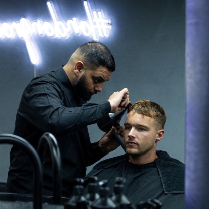 LondonGrooming white Custom Neon® sign on a dark wall above the barber and client