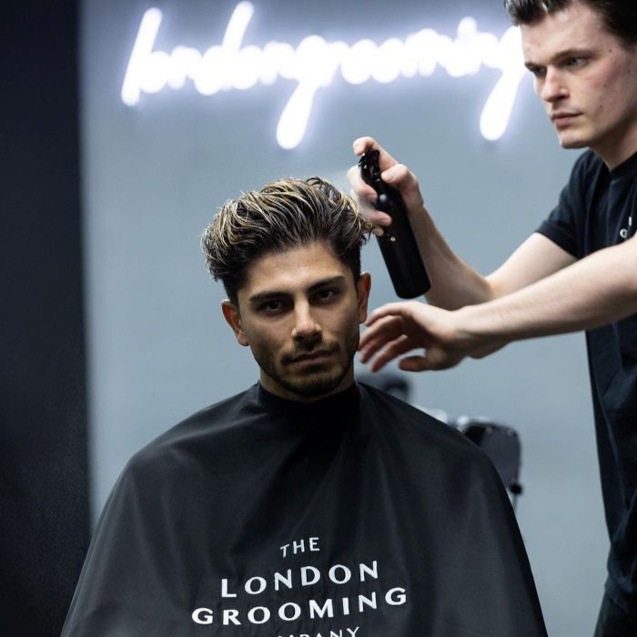 LondonGrooming white Custom Neon® sign on a dark wall above the barber and client