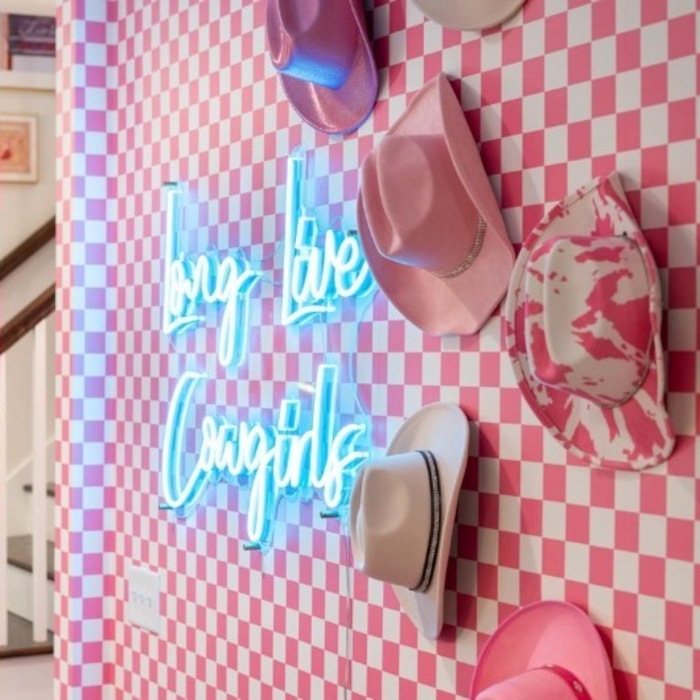 Long Live Cowgirls ice blue LED Custom Neon® sign on pink and whie check wallpaper next to a pink cowgirl hat display designed by Somerled