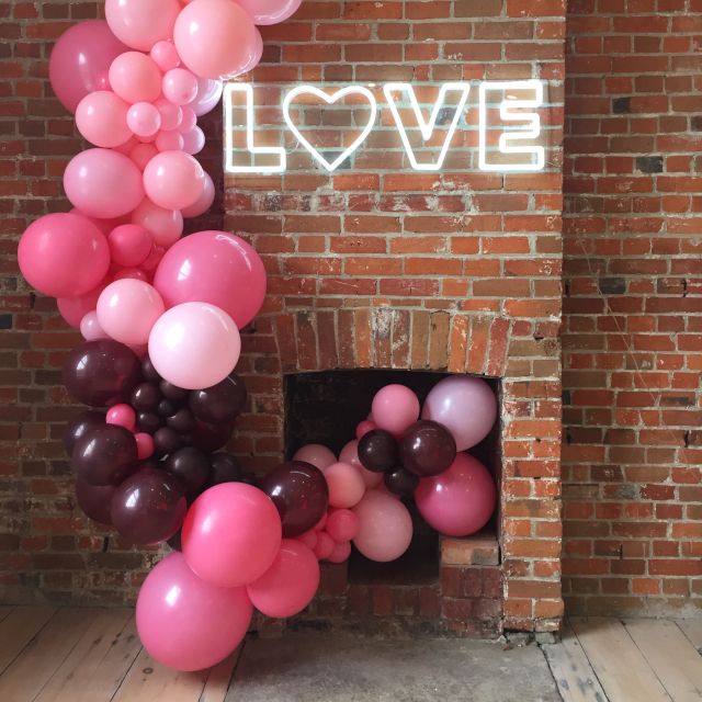 Custom Neon® LOVE sign on a red brick fireplace with a pink balloon garland