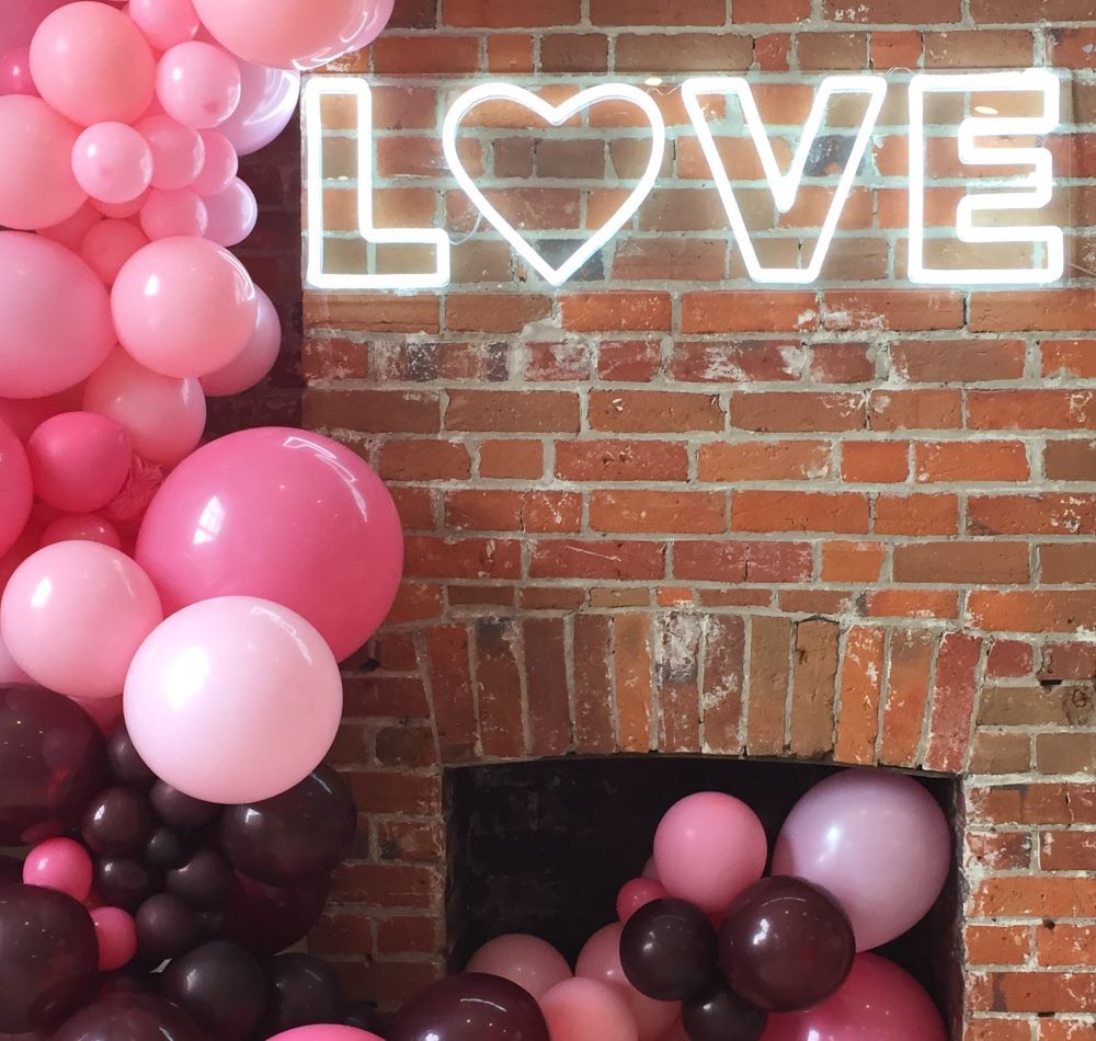Custom Neon® white LOVE sign with a heart mounted on brick fireplace with balloon arch