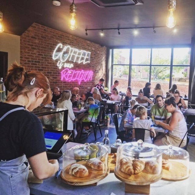 Pink Custom Neon® quote sign Coffee is our Religion on brick wall @mayhapcoffee