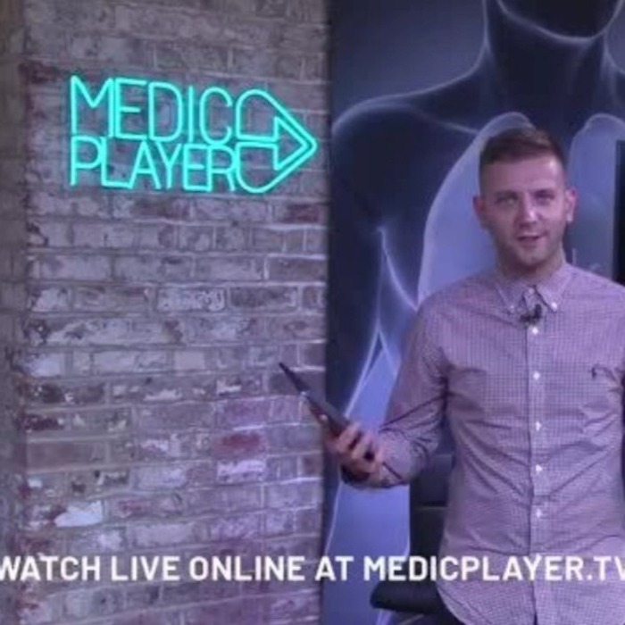 MedicPlayer blue Custom Neon® logo sign on the wall behind the host of a YouTube show