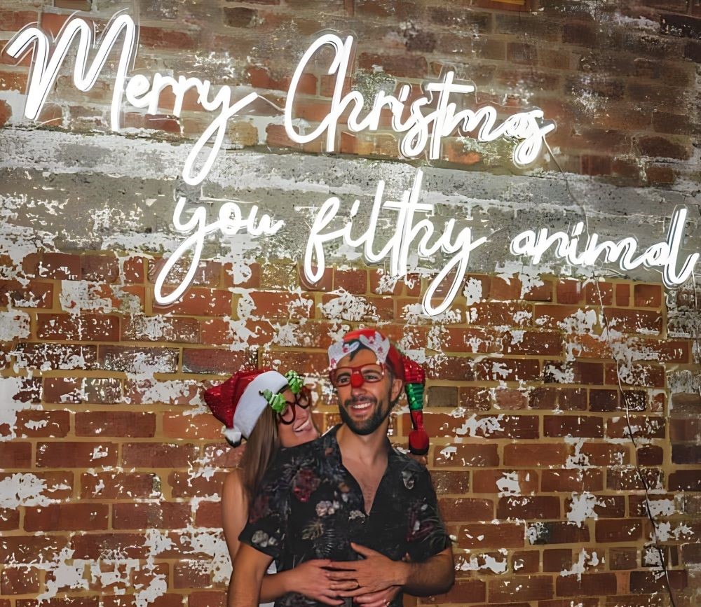 Custom Neon® Merry Christmas you filthy animal Home Alone quote sign on distressed brick wall during a Christmas party