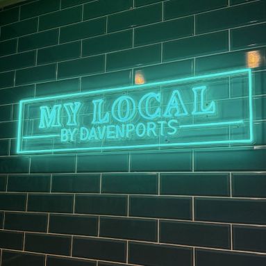 custom LED neon 'My Local by Davenports' sign mounted on a dark green metro-tiled wall