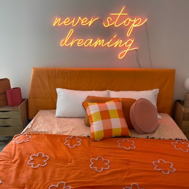 Never Stop Dreaming orange Custom Neon® sign above a bed