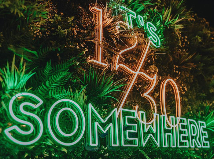 Custom Neon® large green LED neon branded business sign mounted on a plant wall in an open-air bar