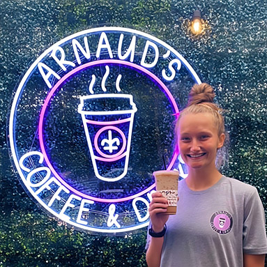 Custom Neon® purple and white circular LED neon coffee shop logo on exterior grasswall