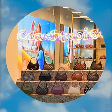 Custom Neon® made Coachtopia logo hanging in the window of a Coach store above the merchandise display