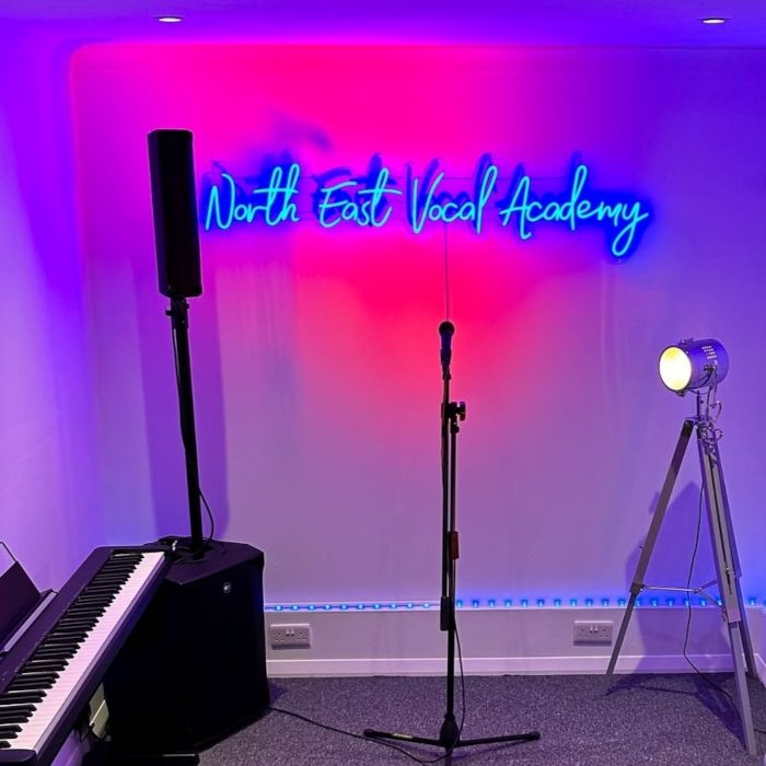 Music room with piano, microphone, spotlight and a dark blue Custom Neon® sign reading North East Vocal Academy as the backdrop