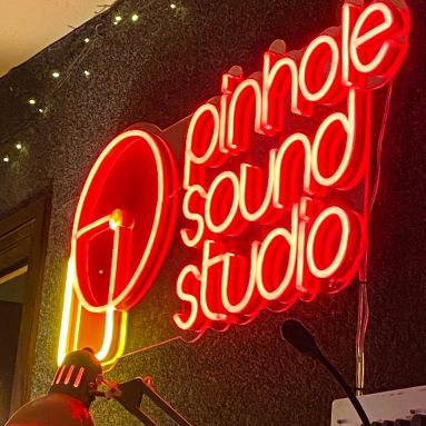 Close-up of the Pinhole Sound Studio red LED neon logo sign with camera icon