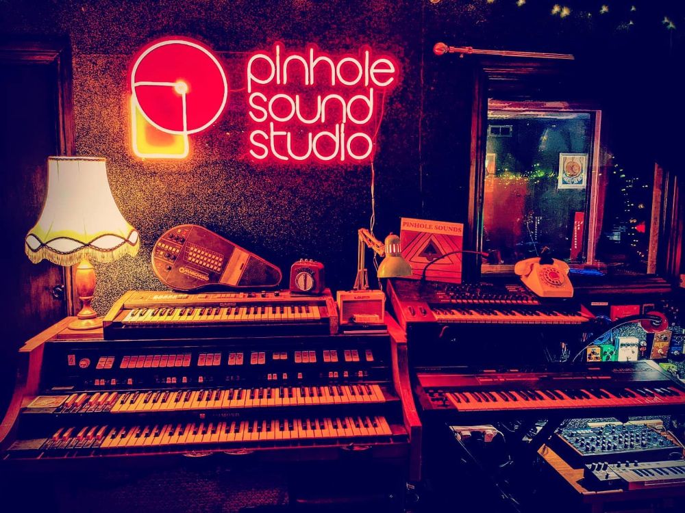 Pinhole Sound Studio red LED neon logo sign above vintage keyboards in a Manchester recording studio