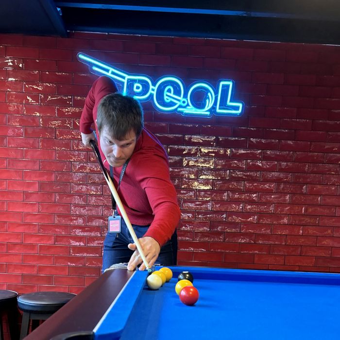 Man playing pool  in front of a blue custom LED neon 'Pool' sign on a red brick wall