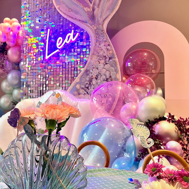Pink Custom Neon® child's name sign on a metallic pink shimmer wall surrounded by mermaid themed decor styled by @rias.room