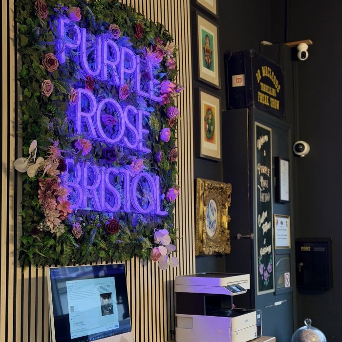 Purple Rose Bristol Custom Neon® sign on a floral greenery wall in the Purple Rose Tattoo studio