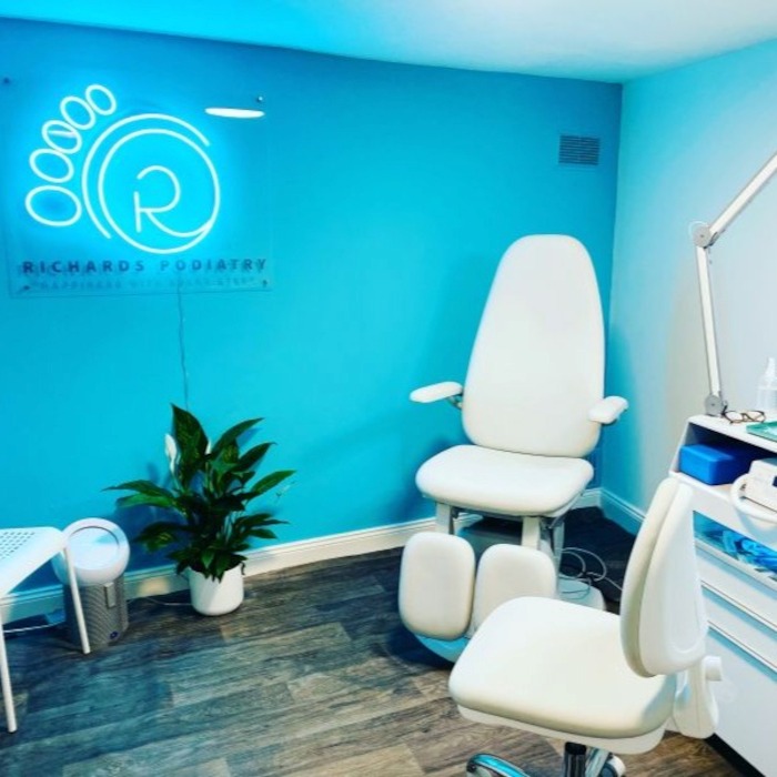 Medical treatment room with white furnishings and a Richards Podiatry Custom Neon® logo sign on a blue wall