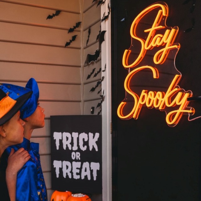 Orange Custom Neon® Stay Spooky sign a black door surrounded by Halloween decorations
