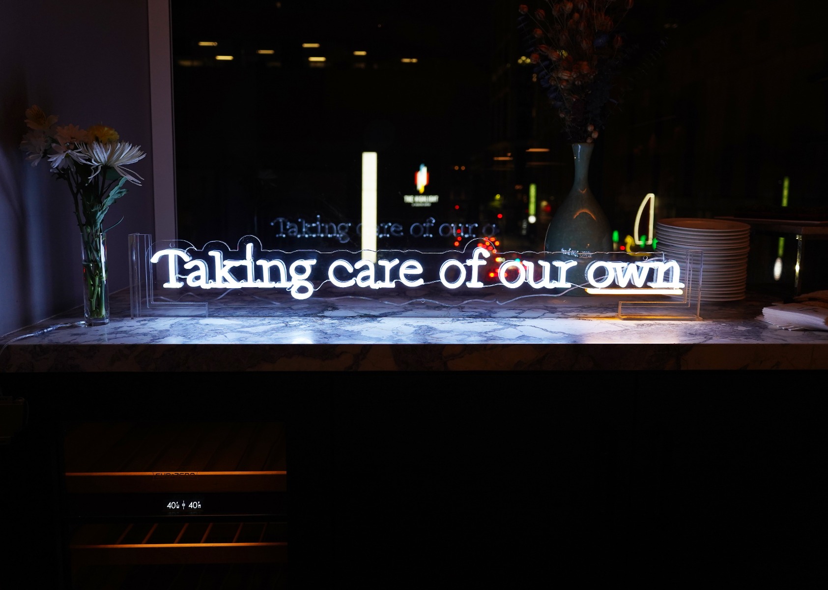 Taking Care of Our Own white Custom Neon® sign in an acrylic stand at a gala event for the Southern Smoke Foundation 