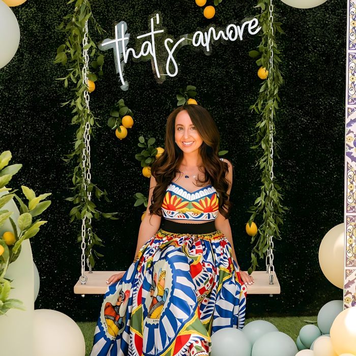 Custom Neon® That's Amore sign on a greenwall festooned with lemons with a lady on a swing in the foreground - event decor by @decorandfiesta