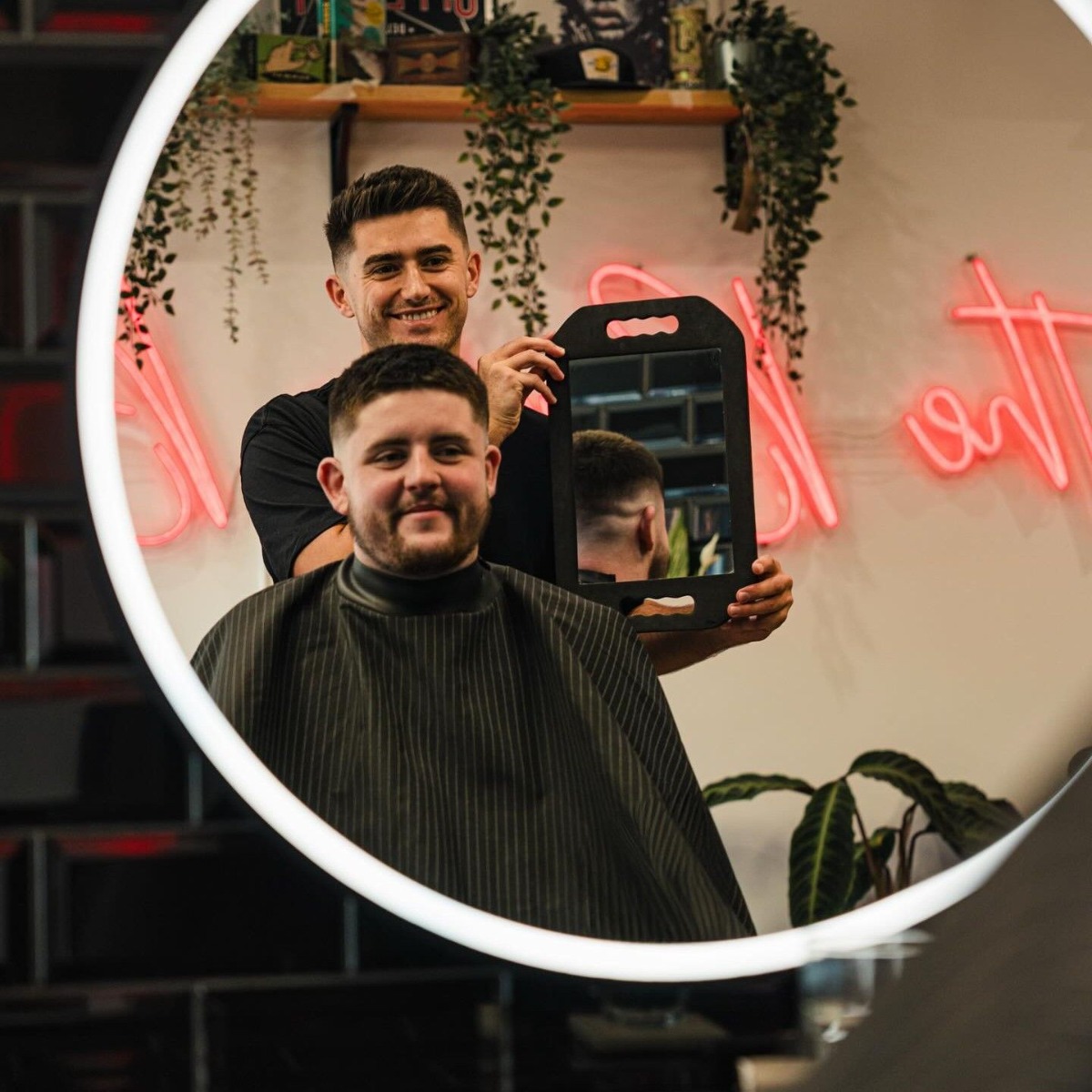 The Barber Brothers red Custom Neon® sign seen in the mirror while a barber shows his client the haircut