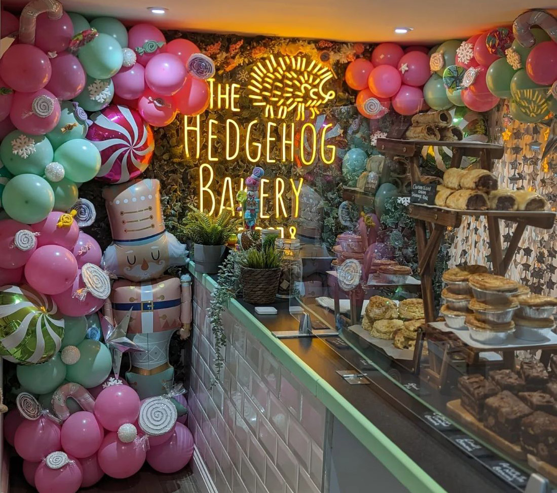 Custom Neon® large retail logo sign surrounded by Christmas balloon garlands and other decorations @thehedgehogbakery