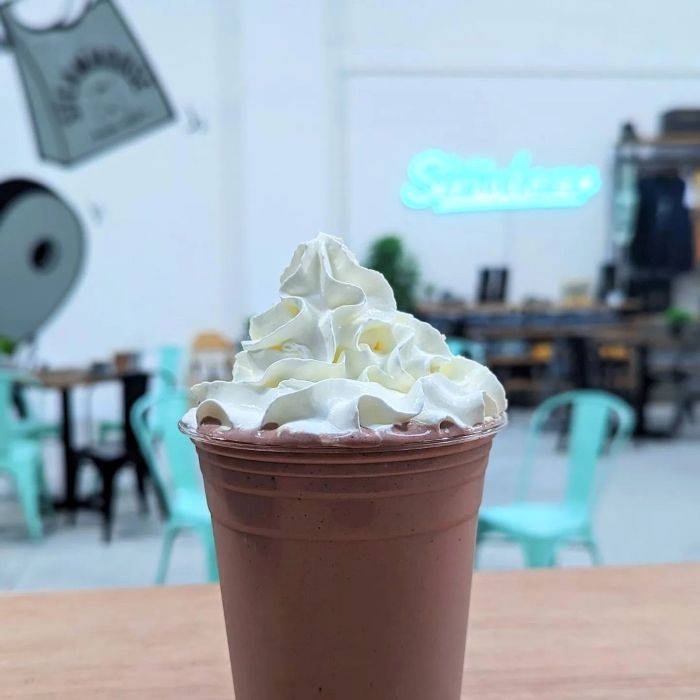 Mint coloured logo on a white wall in the background with an iced coffee on the table in the foreground @thesteamhousebakery