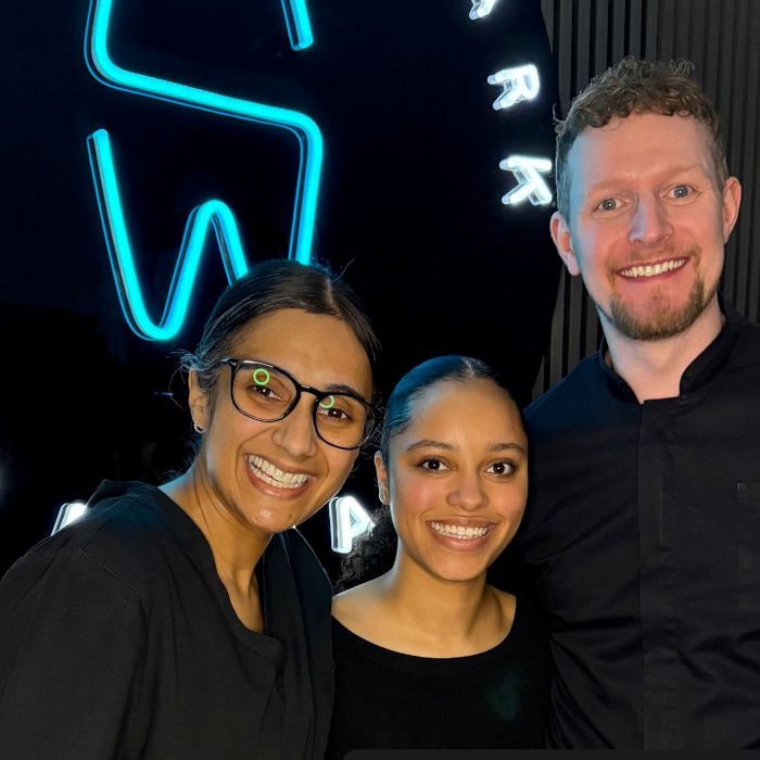 Smiling dental team in front of a blue tooth logo LED neon sign at their Manchester clinic