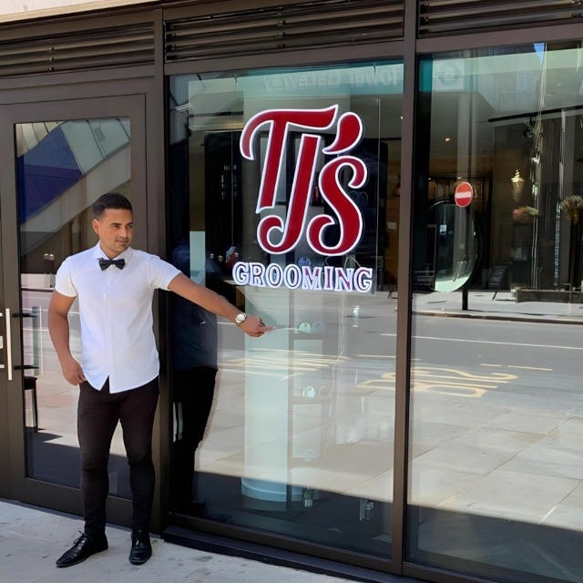 Red and white logo sign in storefront window by Custom Neon® @tjs.grooming