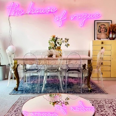 The House of Vogue pink Custom Neon® Airbnb sign on a white wall reflected in the glass coffee table @voguehouse