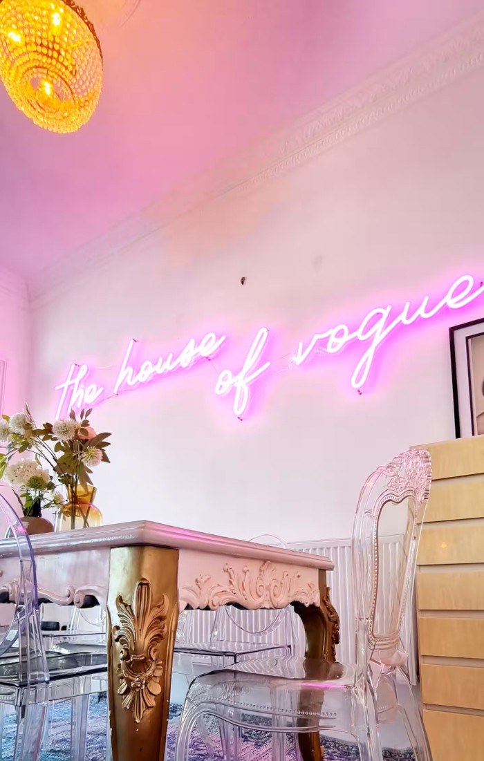 The House of Vogue pink Custom Neon® Airbnb sign on a white wall above the dining table @voguehouse