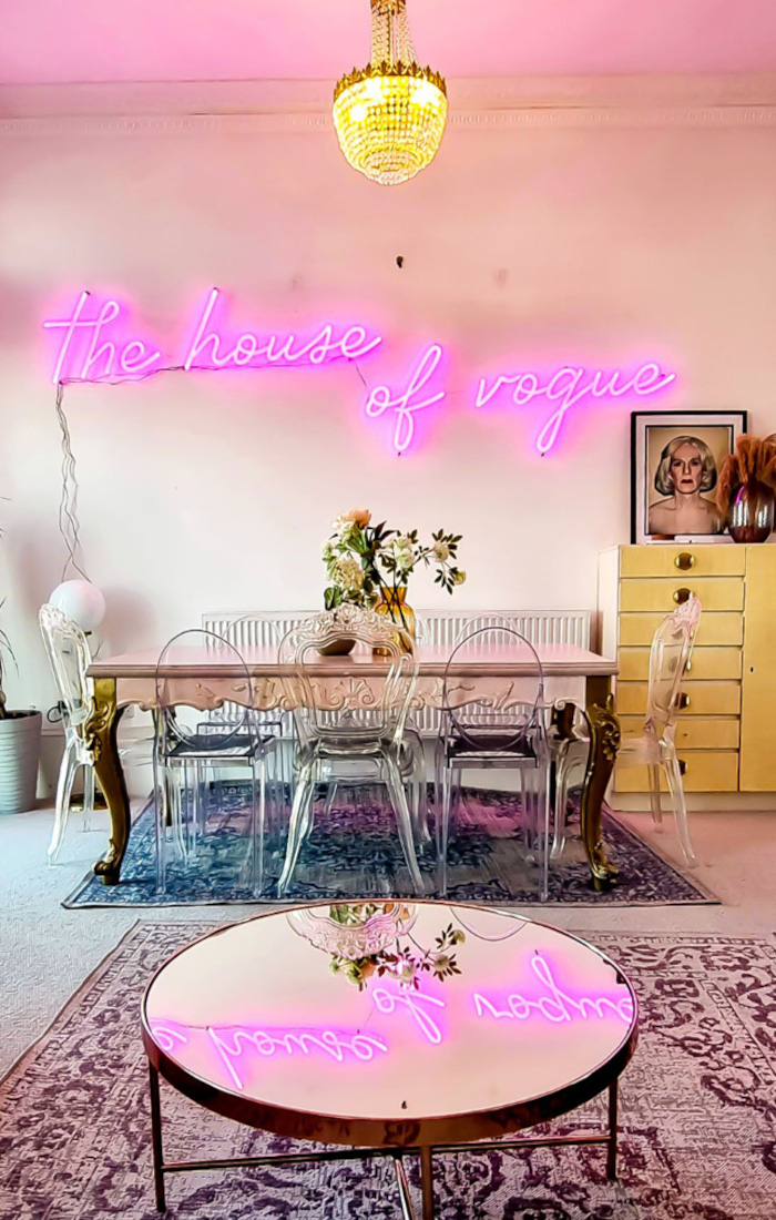 The House of Vogue pink Custom Neon® Airbnb sign on a white wall reflected in the glass coffee table @voguehouse