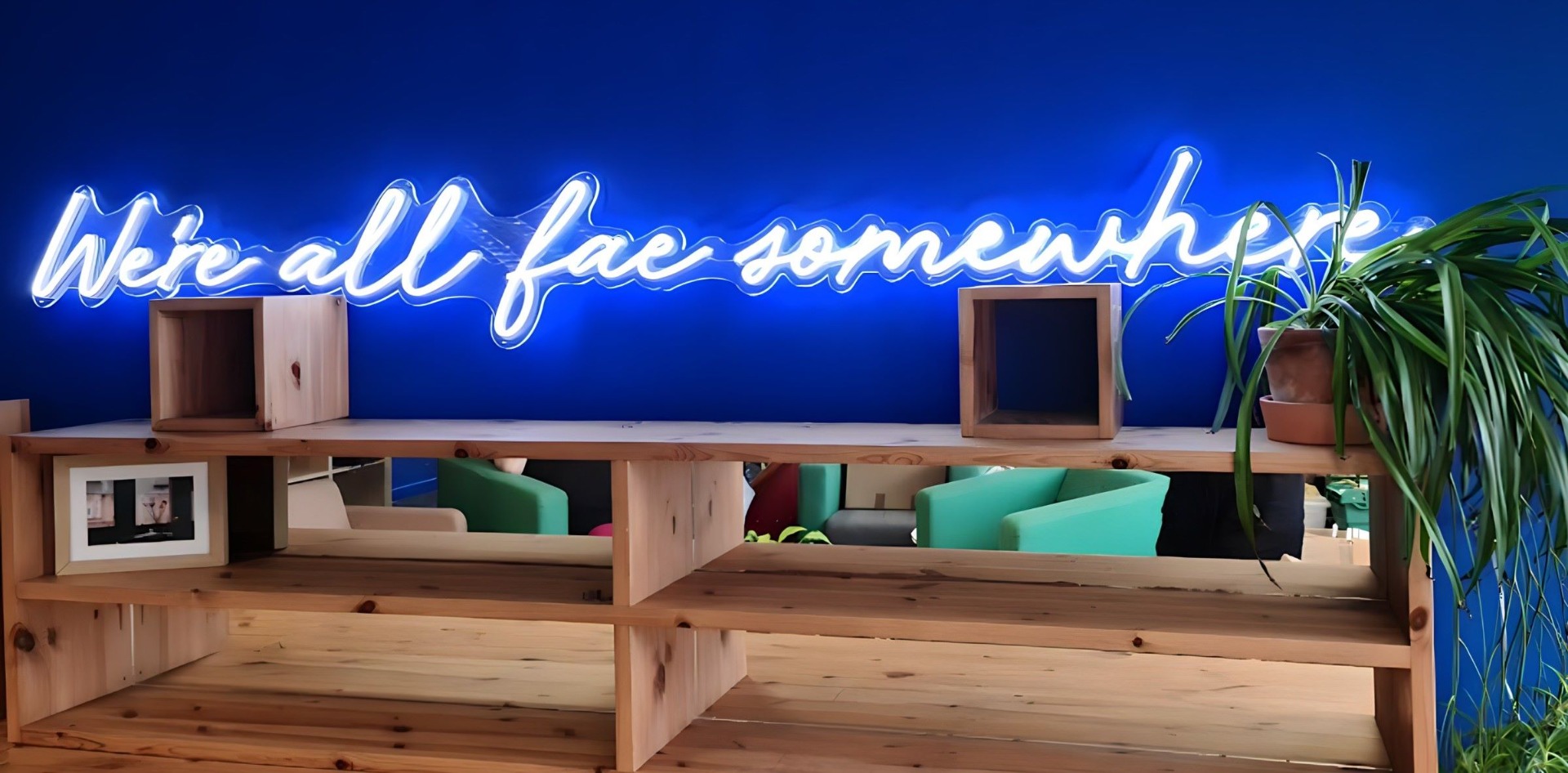 We're all fae somewhere white Custom Neon® quote sign on a blue wall @refuweegee