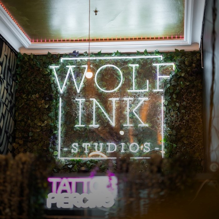 White @wolf_ink_studios logo by Custom Neon® installed against a greenery wall