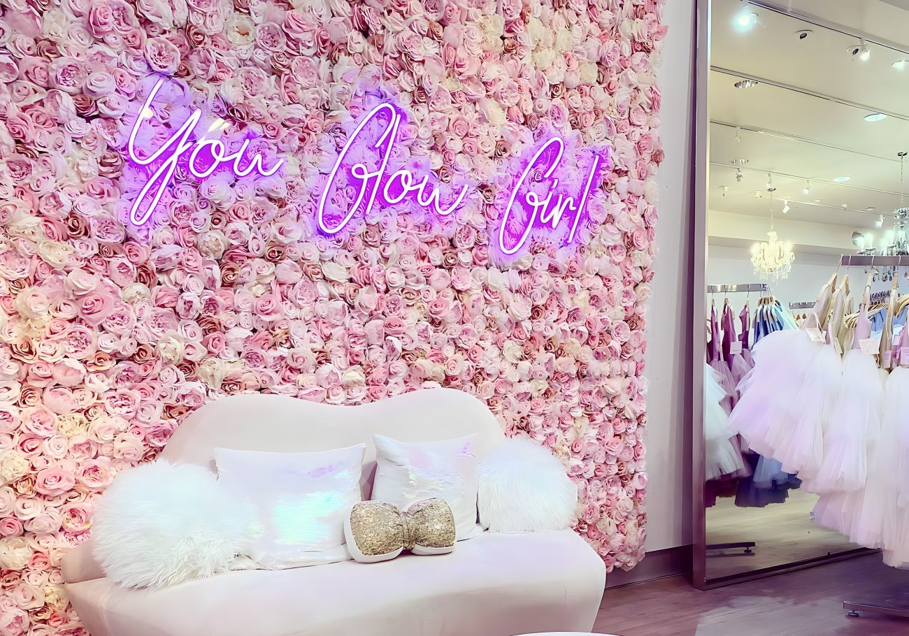 You Glow Girl purple Custom Neon® quote sign on flower wall in a formal dress shop @michellewalshdesigns